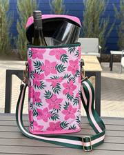 Pink floral patterned cooler bag with bottle and glasses on a wooden table outdoors.