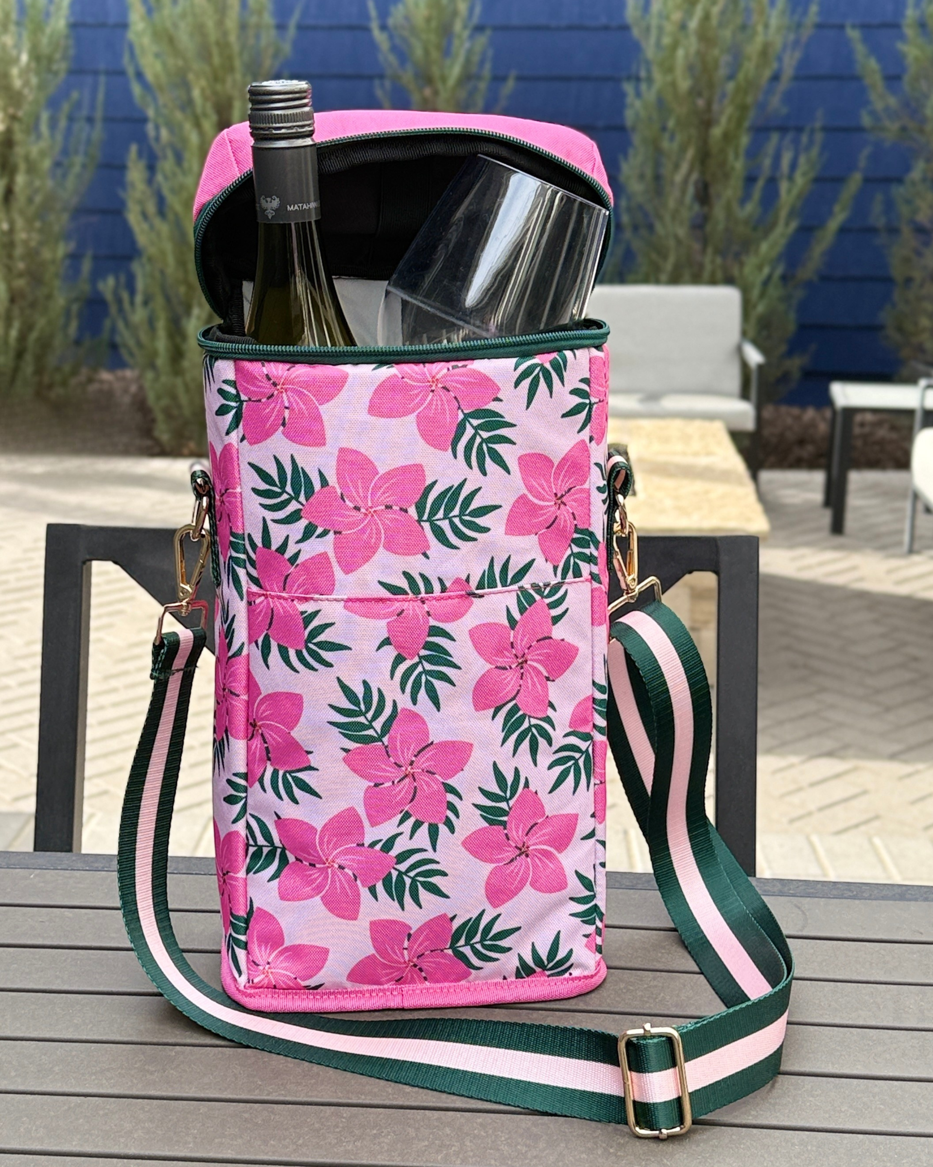 Pink floral patterned cooler bag with bottle and glasses on a wooden table outdoors.
