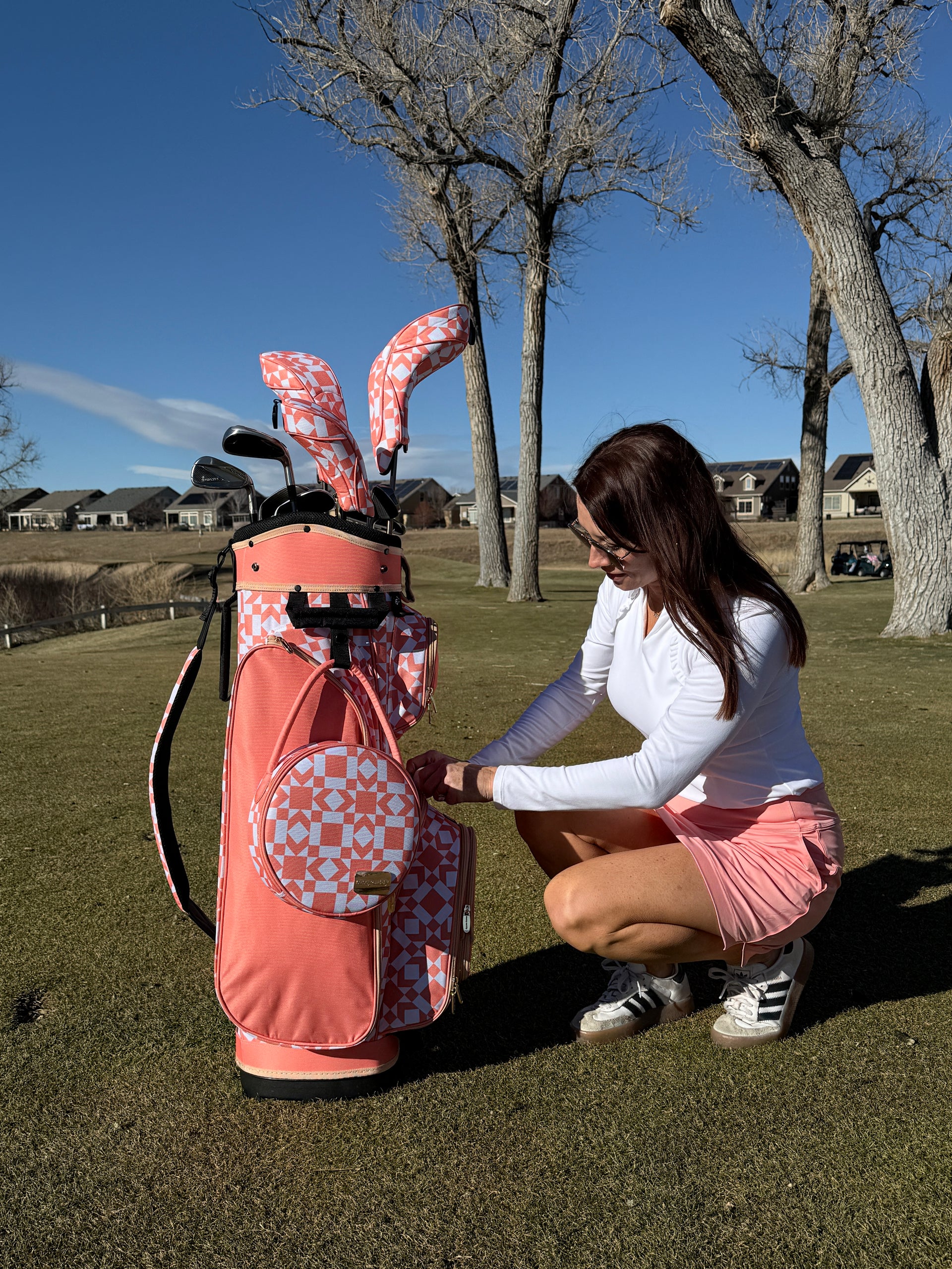 Woman in a pink outfit interacting with a golf bag on a golf course.