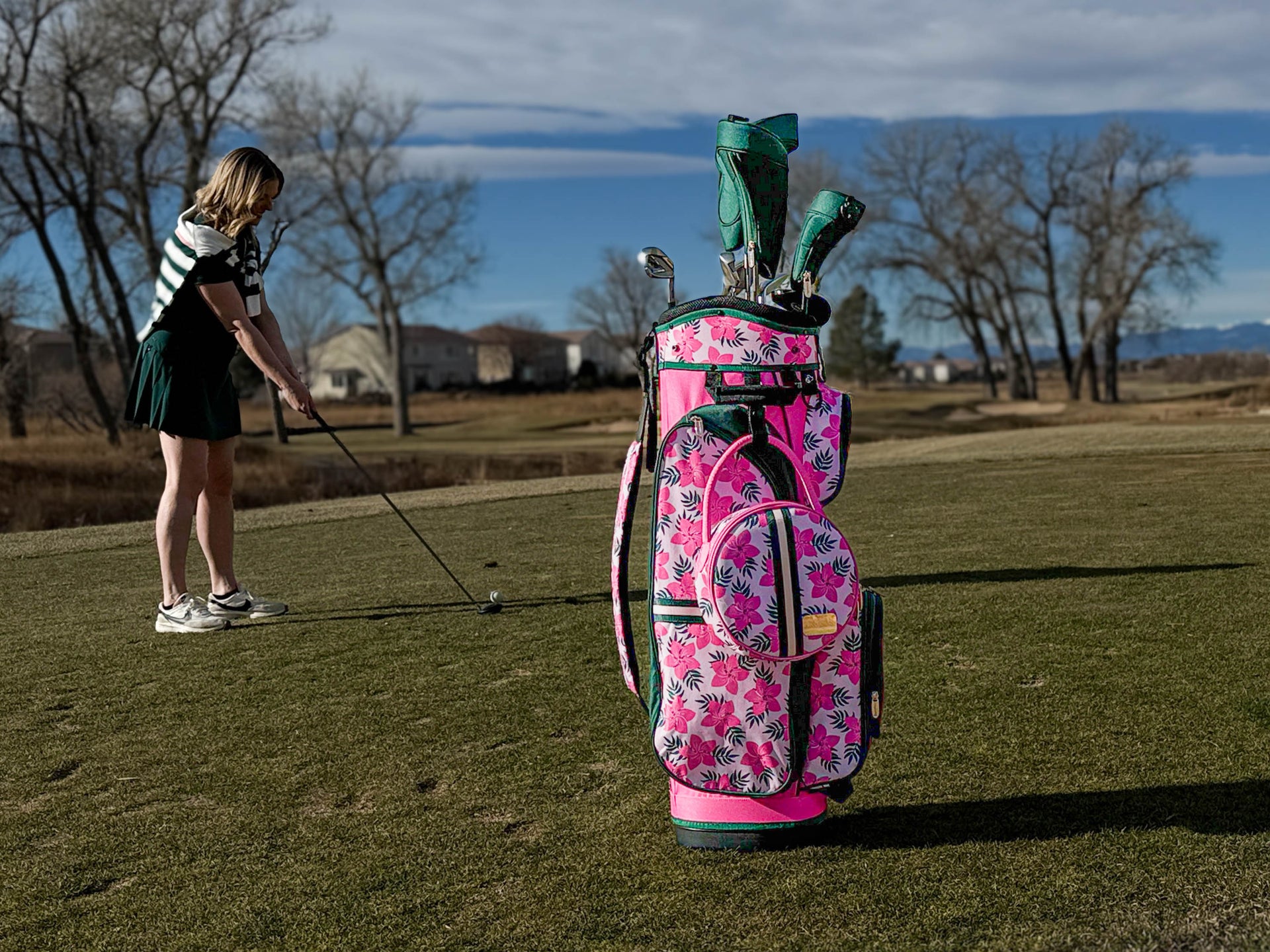 Woman practicing golf on a course with a pink floral golf bag.