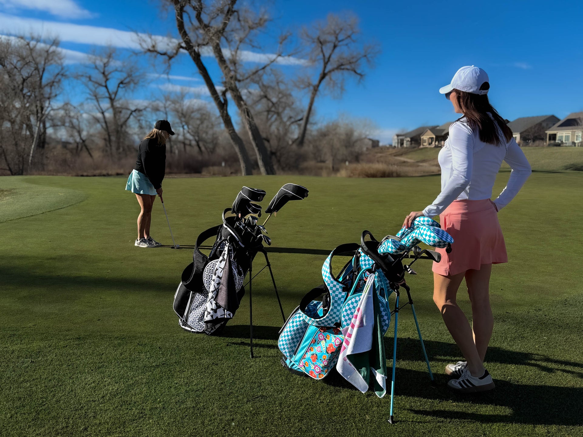 Two women on a golf course with golf bags and clubs.