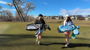 Two women walking on a golf course with golf bags.